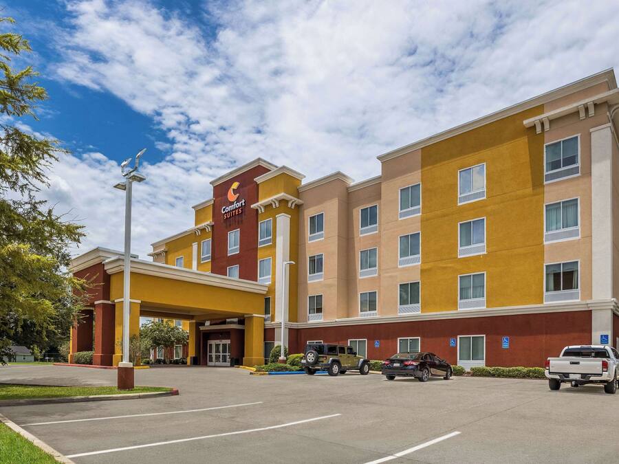 A hotel with a yellow and brown facade, multiple windows, and a parking lot with several vehicles.