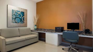 A modern office space with a beige sofa, a desk with a computer, and a TV.