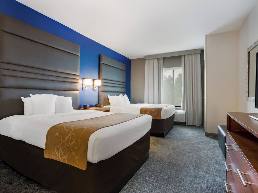 A hotel room with two beds, a desk, a TV, and a window with curtains.