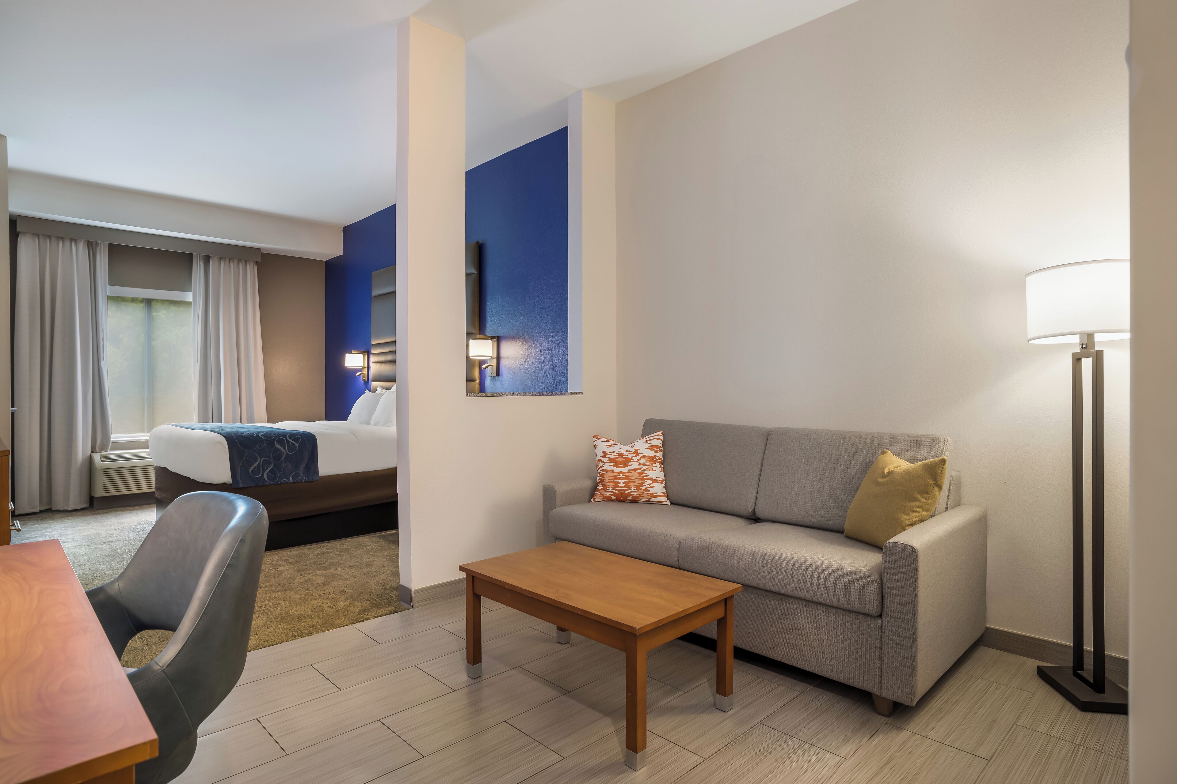Una habitación de hotel con una cama, un sofá, una mesa de centro, un escritorio y una lámpara.