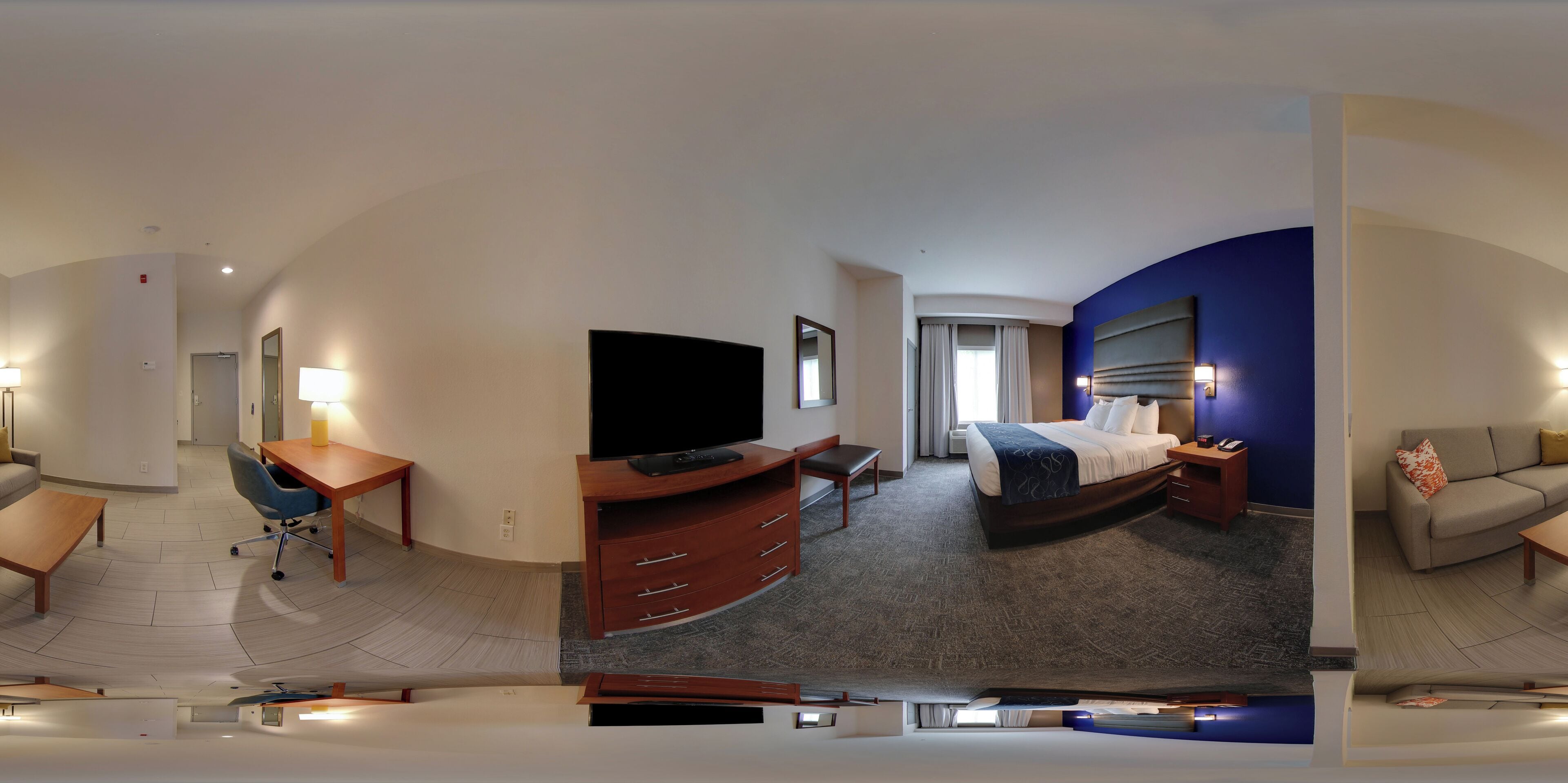 Quarto de hotel com cama, escrivaninha com cadeira, televisão, sofá e banheiro.