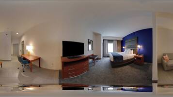 Quarto de hotel com cama, escrivaninha com cadeira, televisão, sofá e banheiro.