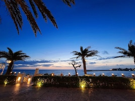 Un paseo marítimo a última hora con palmeras, vista al mar y senderos iluminados.