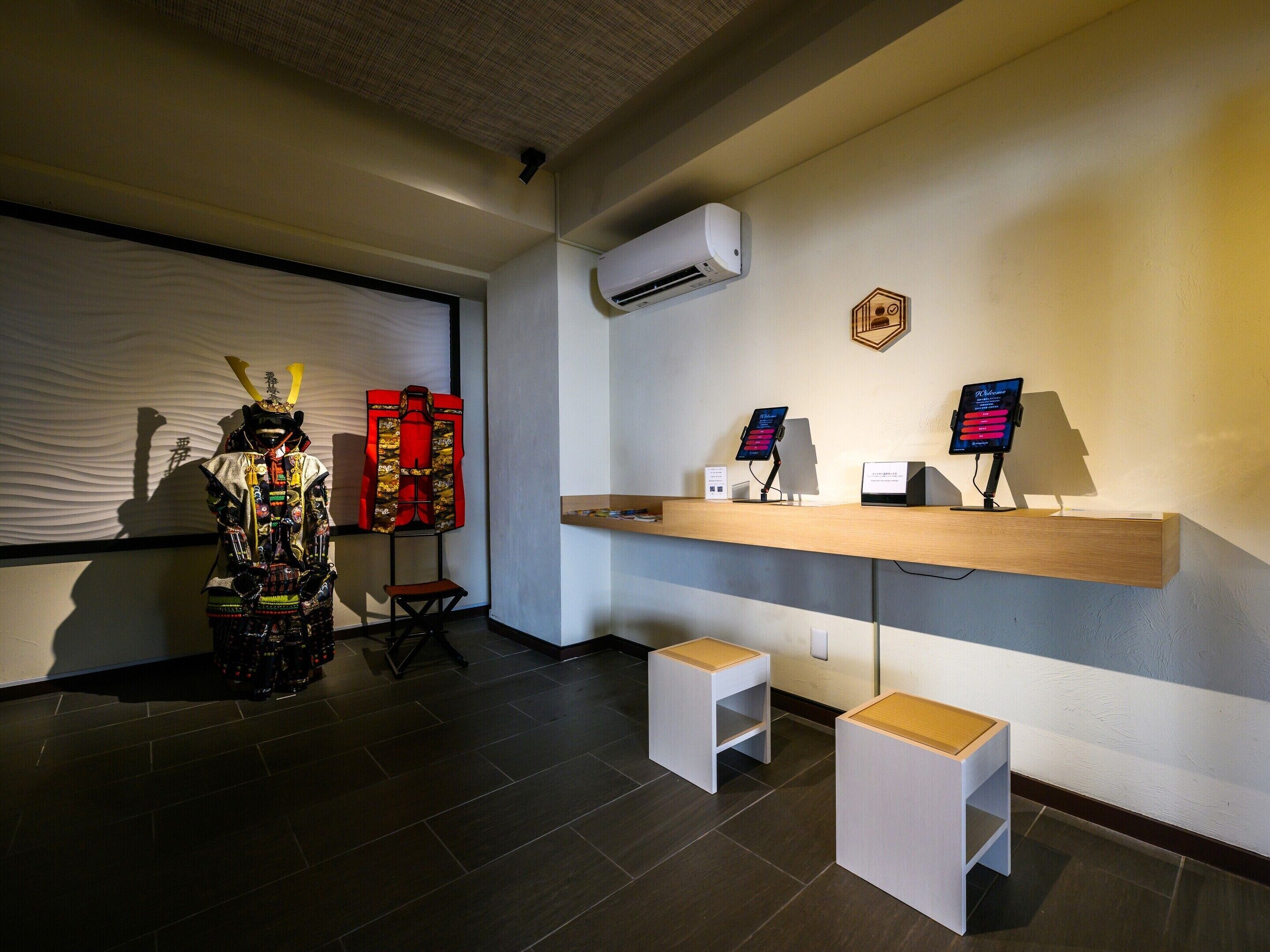 A reception area with a mannequin dressed in traditional attire, a red jacket on a stand, a wooden reception desk with a digital screen, and a small white stool.