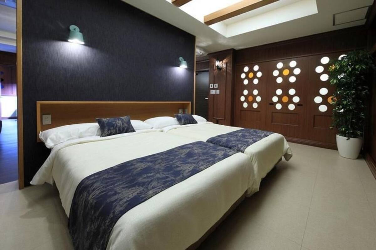 Ein Hotelzimmer mit einem großen Bett, einem Holzkopfstück, einer Wand mit runden Leuchten und einer Zimmerpflanze.