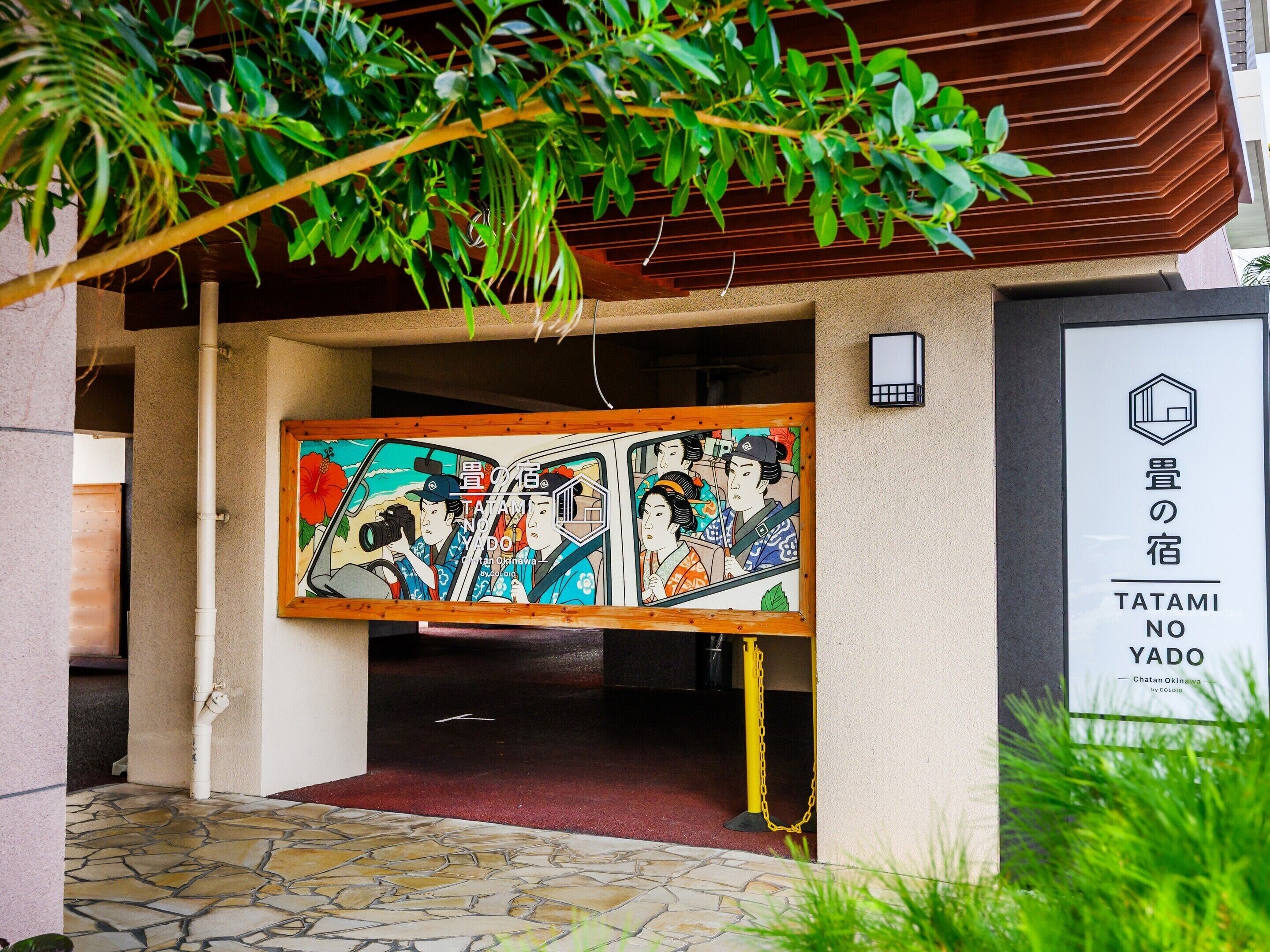 Entrada de un edificio japonés tradicional con un gran cuadro colorido de figuras históricas, suelo de losas de piedra y un letrero que indica el nombre 'TATAMI NO YADO'.