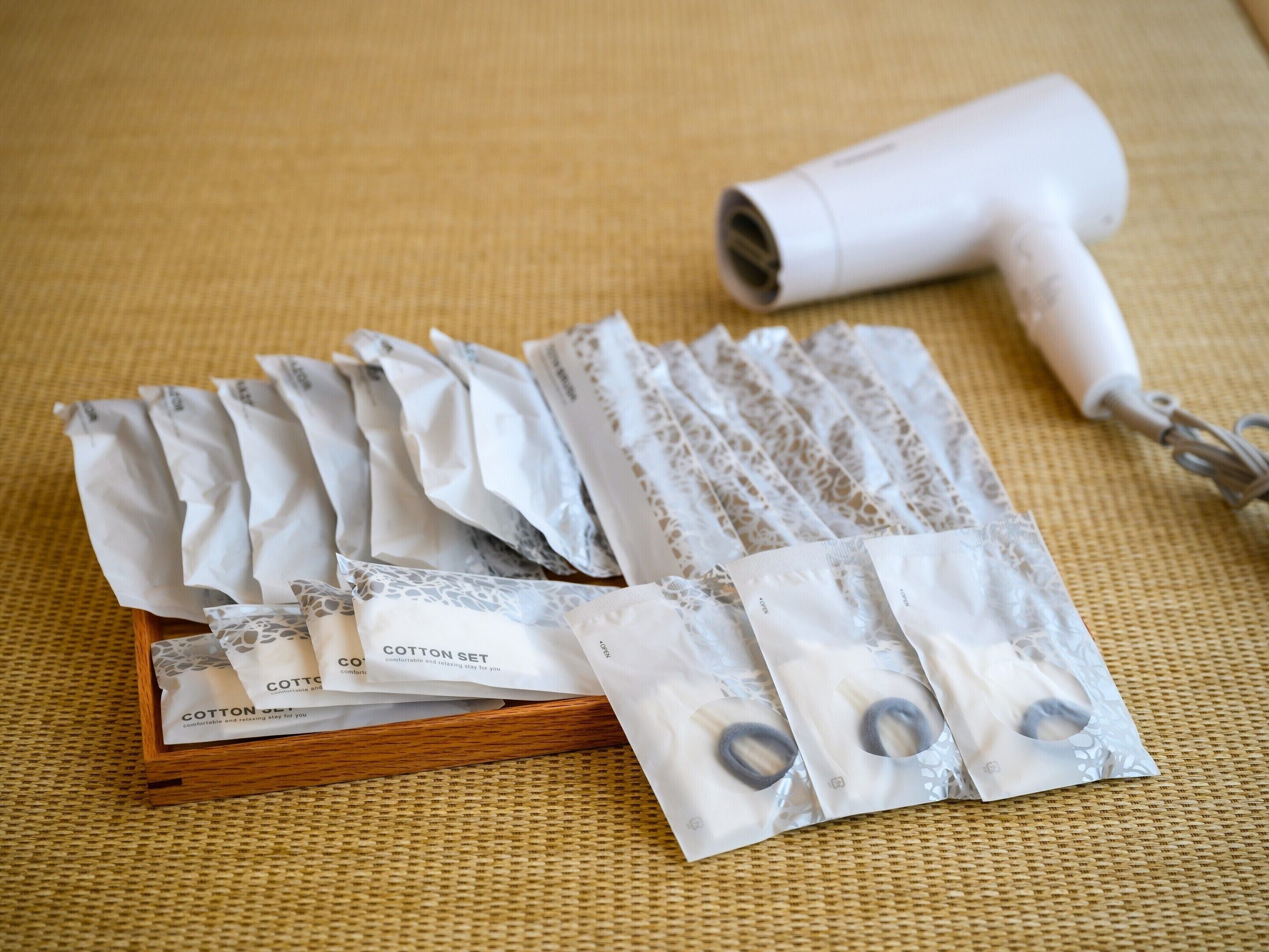 A wooden box containing multiple cotton sets and a white hair dryer on a woven mat.