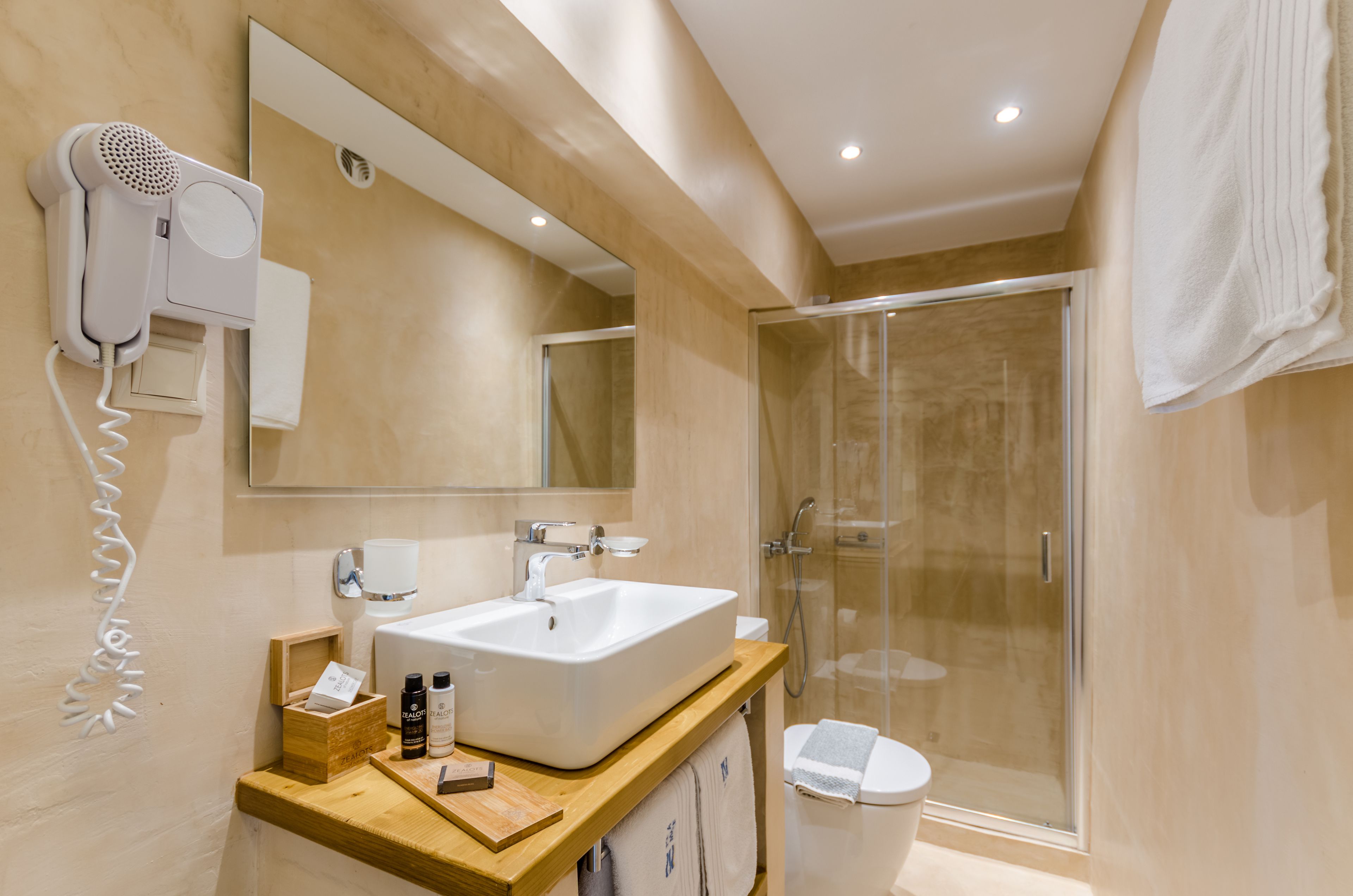 A modern bathroom with a large mirror, a white sink, a hairdryer, and a glass-enclosed shower.