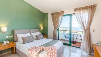 Habitación de hotel con cama, lámparas de noche, teléfono, balcón con una silla y vista al mar.