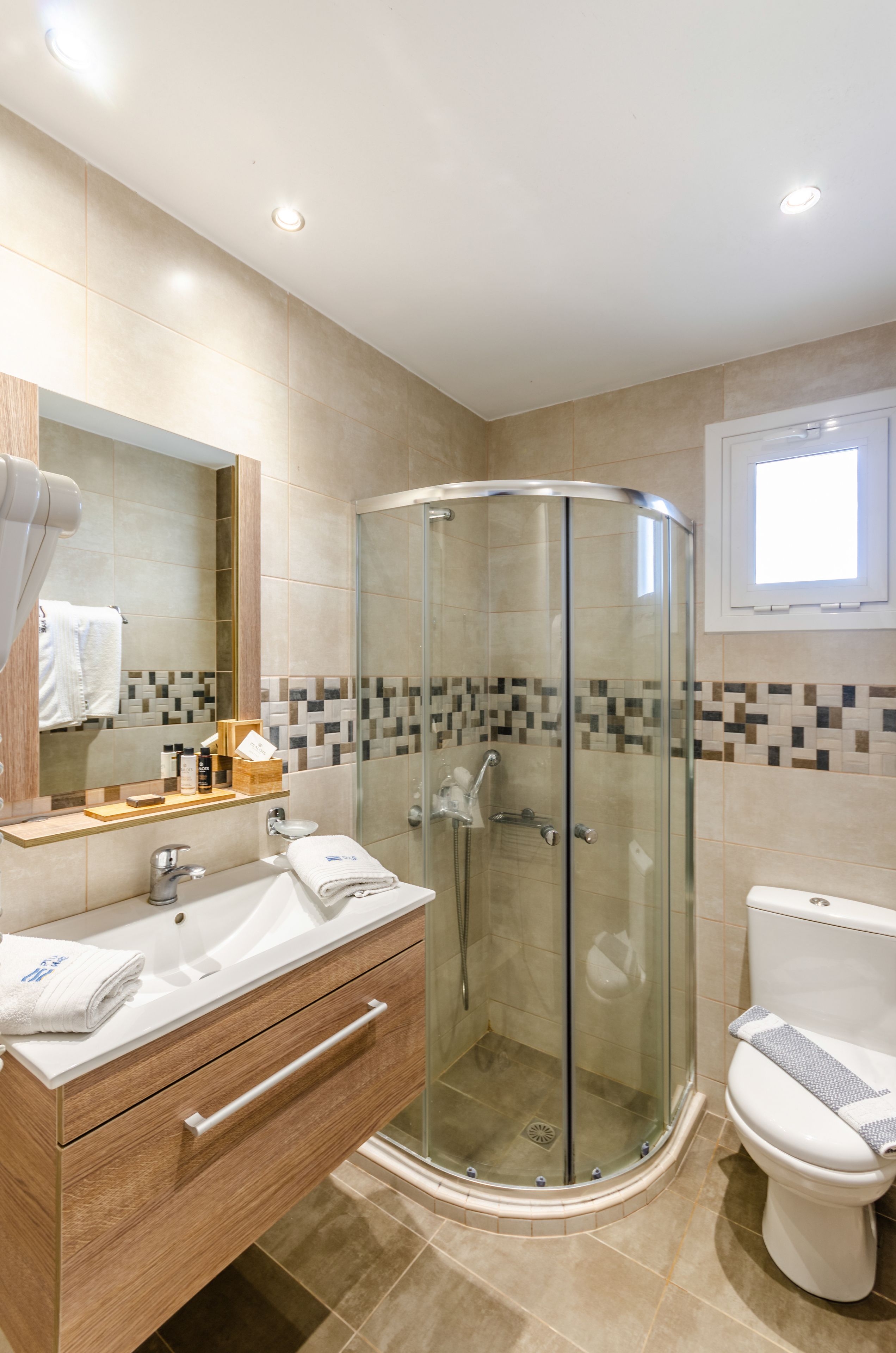 Une salle de bain moderne avec une douche à parois de verre, un meuble-lavabo en bois avec un évier et un miroir, et des toilettes avec une serviette posée sur la lunette.