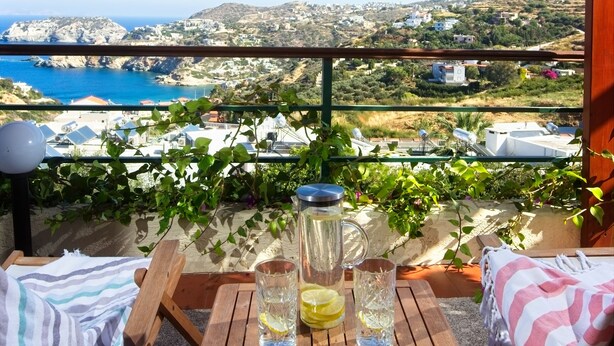 A wooden table with drinks and lemons, overlooking a coastal landscape with houses and hills. - Pela Mare Hotel (Malevizi)