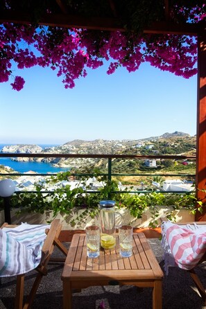 A wooden table with drinks and lemons, overlooking a coastal landscape with houses and hills. - Pela Mare Hotel (Malevizi)