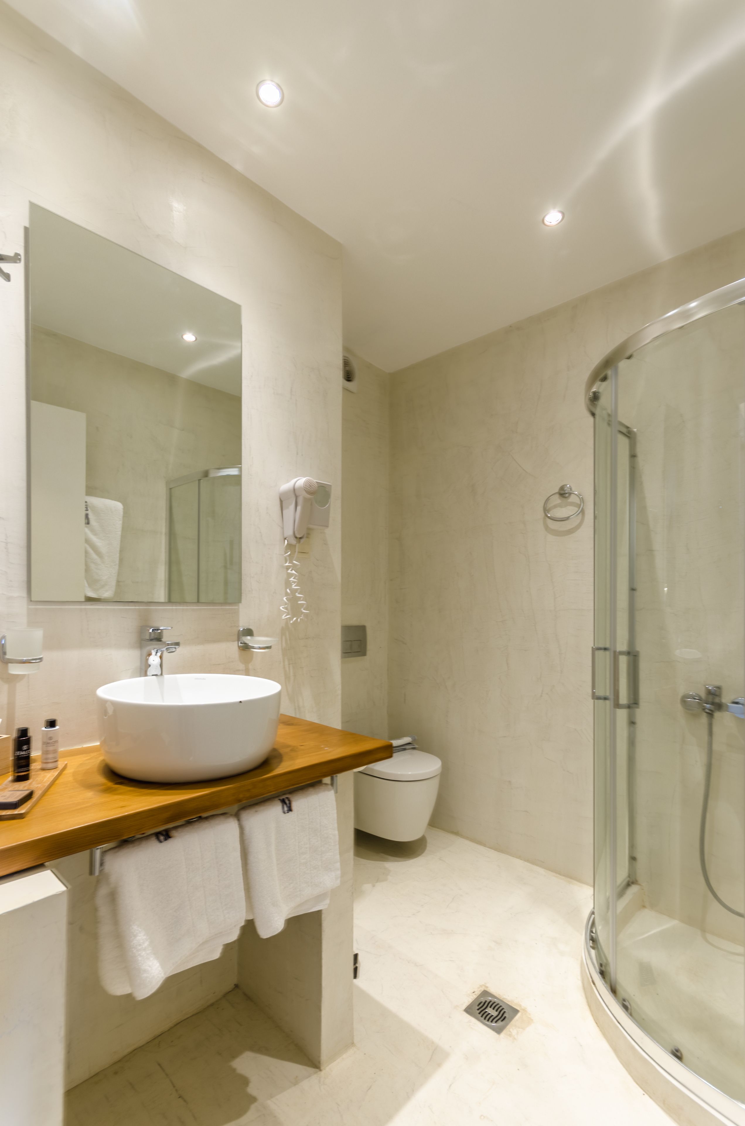 Un bagno moderno con un lavandino capiente, uno specchio, un asciugacapelli e una cabina doccia in vetro.