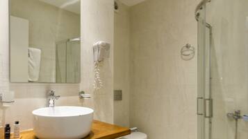 Un bagno moderno con un lavandino capiente, uno specchio, un asciugacapelli e una cabina doccia in vetro.