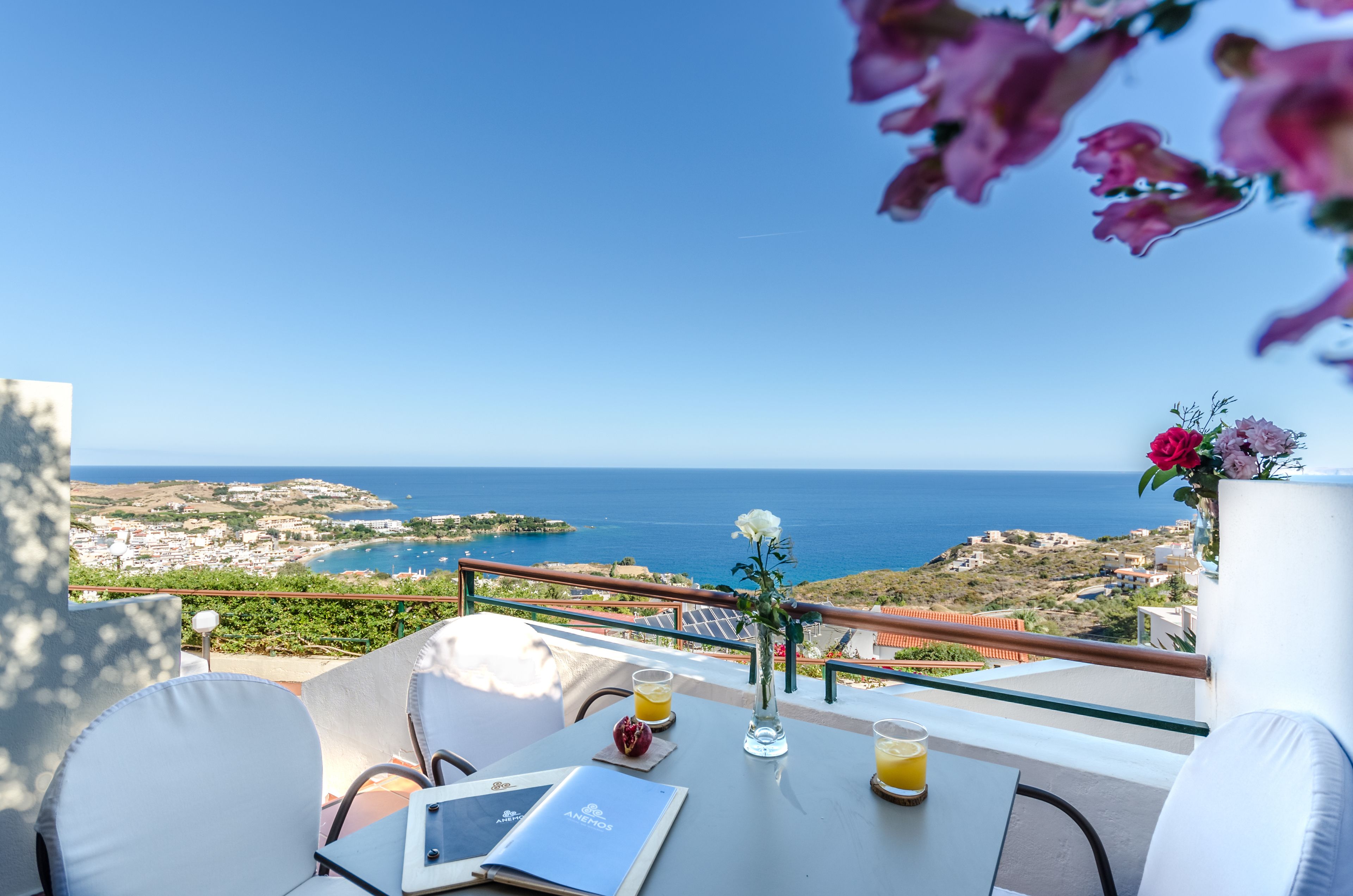 Una terraza con mesa, sillas, un florero con flores y vistas al mar y al paisaje.