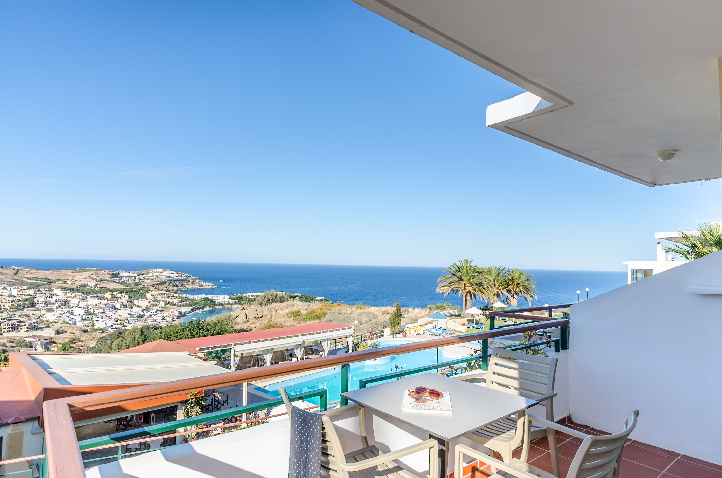 Un balcon avec une table et des chaises donnant sur une piscine et la mer.