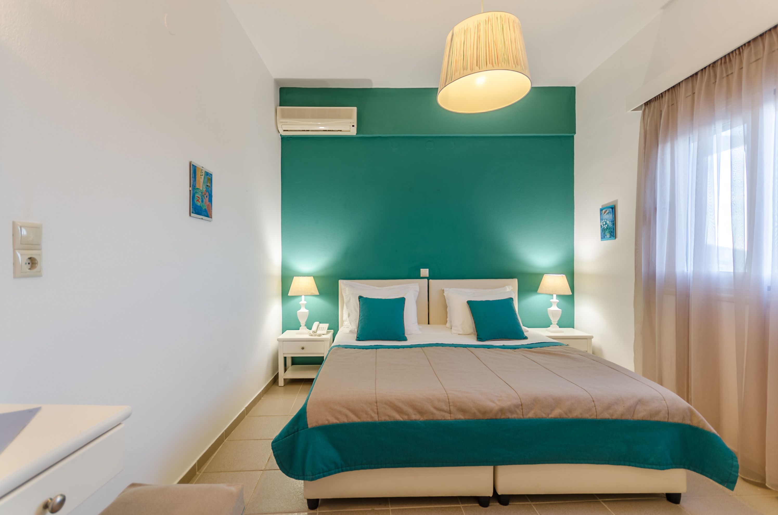 A bedroom with a bed, nightstands, a lamp, an air conditioner, and a window with curtains.