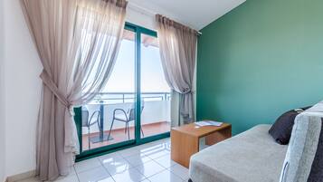 A hotel room with a bed, a small wooden table, a chair, and a balcony with a view.