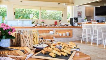 Een ontbijtbuffet met diverse gebakjes en brood, een koffiehoek, en uitzicht op het omliggende landschap door grote ramen.
