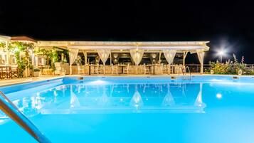 Uma área de piscina à noite, com um espaço de estar coberto e piscina transparente.