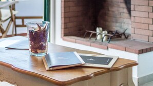 A table with a glass of drink and a book, a fireplace, and a view of the outdoors. - Pela Mare Hotel (Malevizi)
