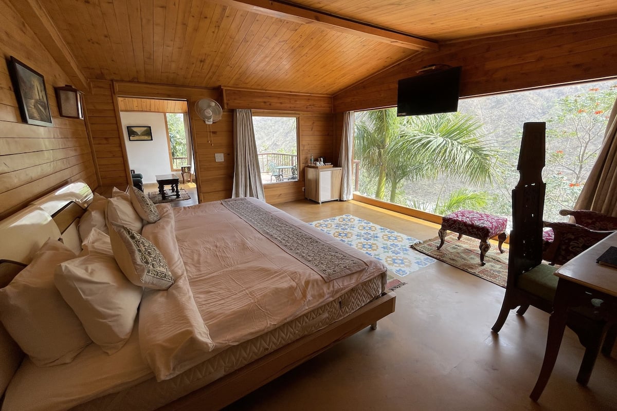 A wooden cabin bedroom with a large bed, a desk, and a television.