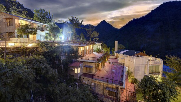 A modern multi-story building with balconies and terraces, surrounded by lush greenery and mountains. - Raga on the Ganges (Narendranagar)