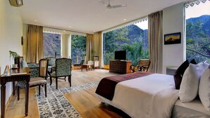 A spacious bedroom with a large bed, a seating area with chairs, a television, and a view of a mountainous landscape. - Raga on the Ganges (Narendranagar)