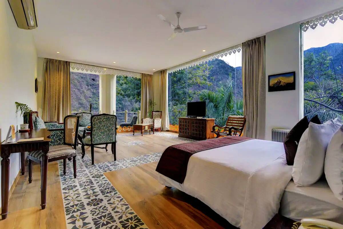 A spacious bedroom with a large bed, a seating area with chairs, a television, and a view of a mountainous landscape.