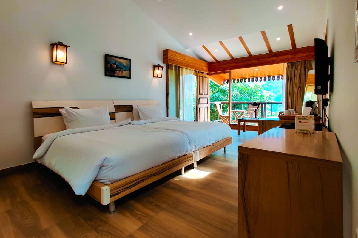 A bedroom with a bed, wooden floor, ceiling fan, and a balcony with a table and chairs.