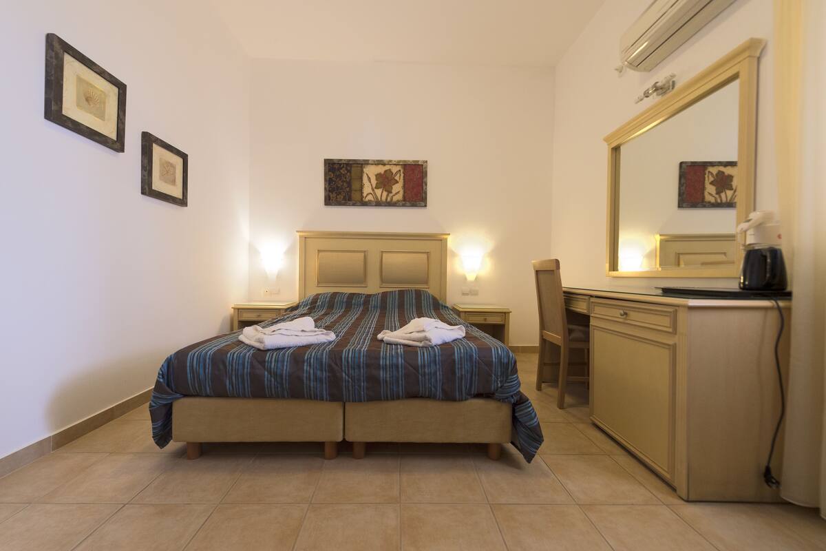 A hotel room with a bed, bedside tables, a desk, a mirror, and artwork on the walls.