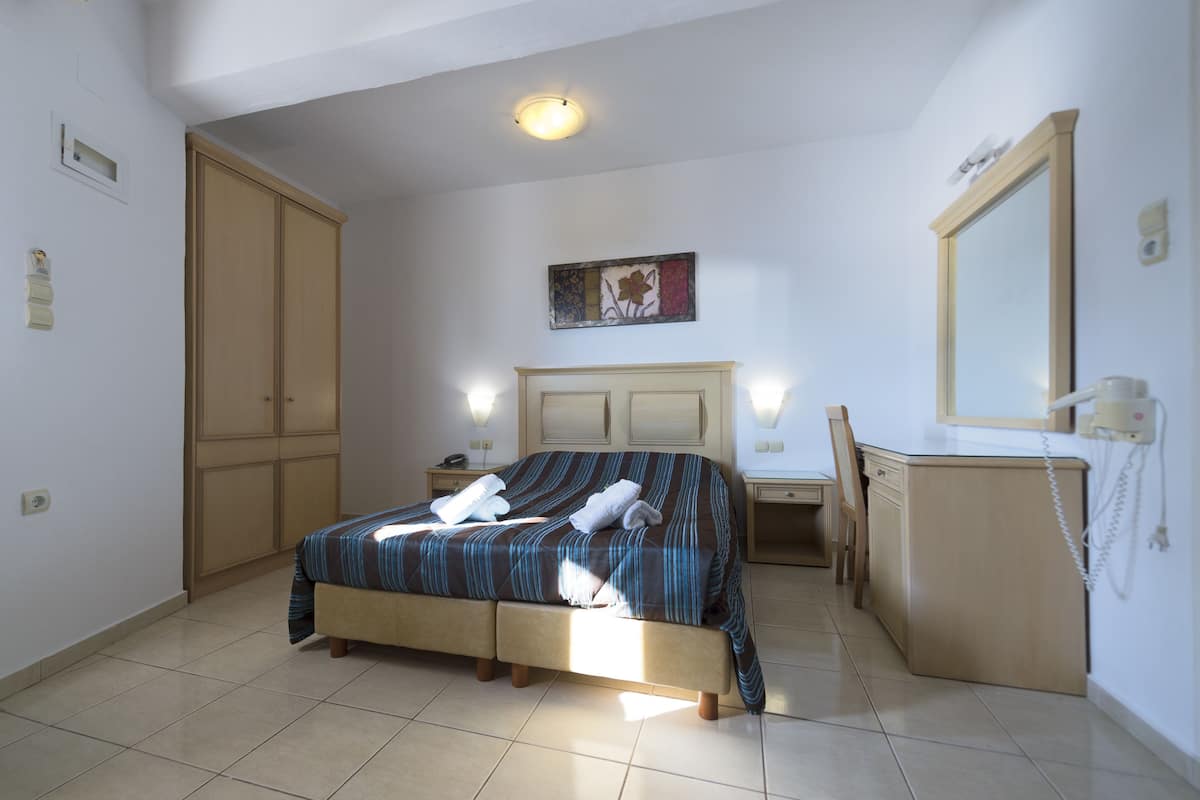 A bedroom with a bed, bedside tables, a desk, a chair, a wardrobe, and a mirror.