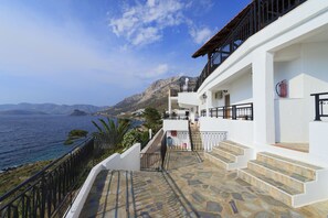 A white building with a stone staircase leading to a balcony overlooking the sea.