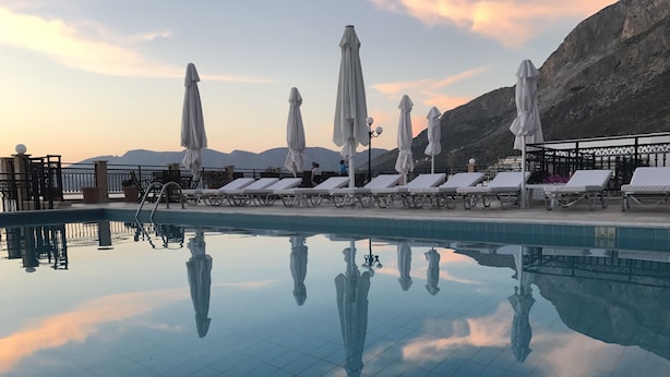 Una piscina con sillas de descanso y sombrillas, rodeada de montañas.