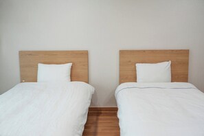 Two single beds with wooden headboards and white bedding in a room with a plain wall and wooden flooring. - MONA YongPyong Resort (Pyeongchang)