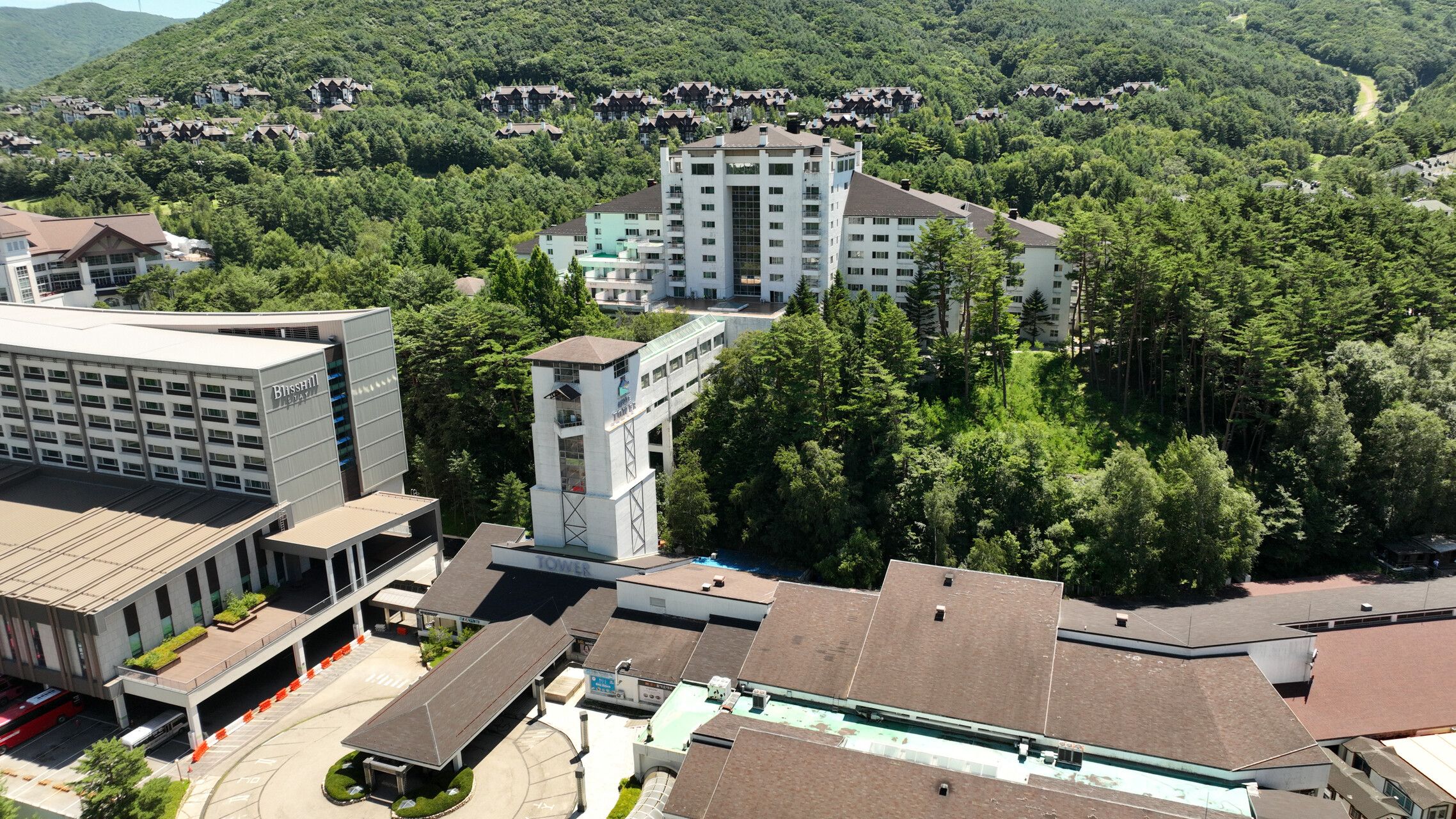A multi-story hotel with a central tower, surrounded by dense forest.