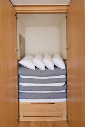 Un armario de madera con una cama en su interior, con varios almohadones y un colchón gris.