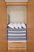 Un armario de madera con una cama en su interior, con varios almohadones y un colchón gris.