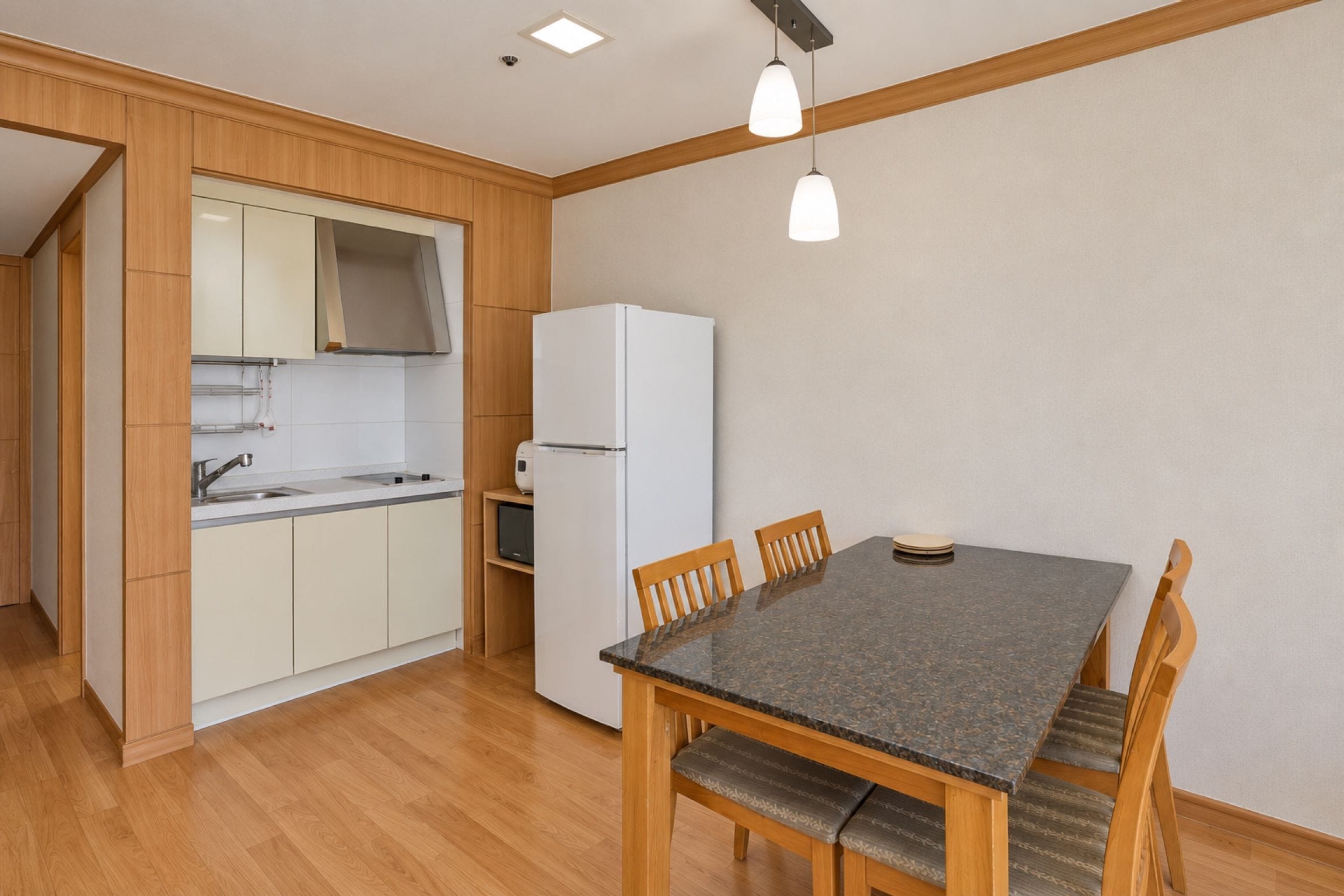 A compact kitchen with a dining area, wooden cabinets, a white refrigerator, and a table with chairs.