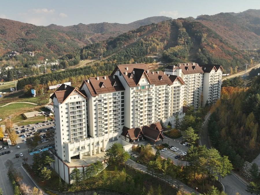 Un hôtel à plusieurs étages doté d’une cour intérieure, entouré d’un paysage montagneux et d’un feuillage automnal.