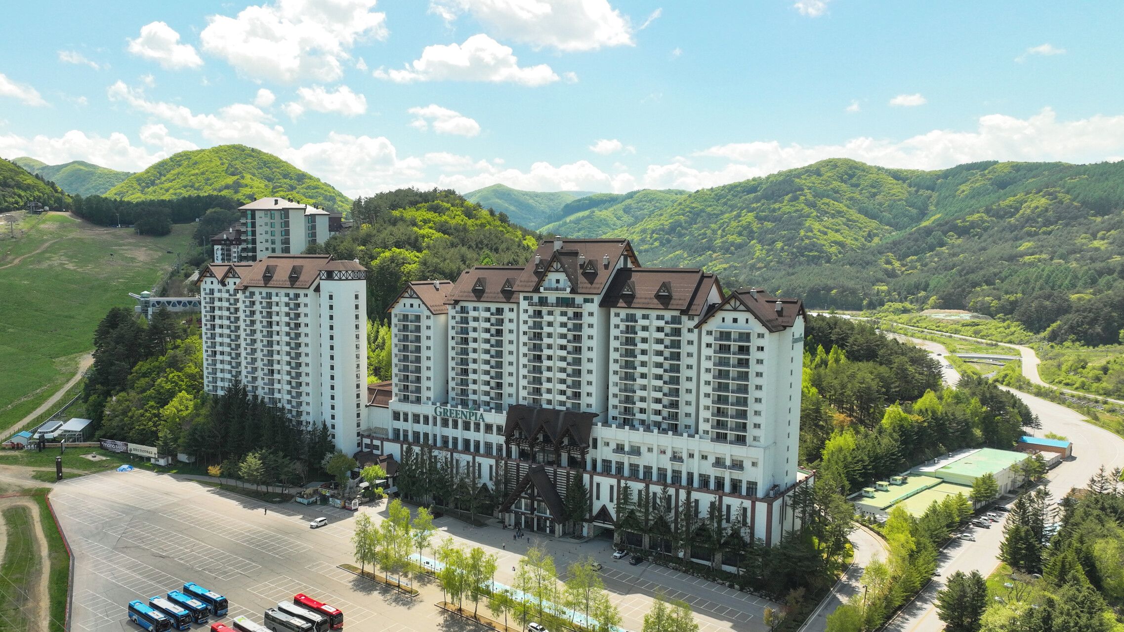 A multi-story hotel with a central courtyard, surrounded by lush greenery and hills.