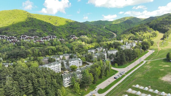 Un quartier résidentiel composé de plusieurs immeubles d’appartements, entouré d’une forêt dense et de collines.