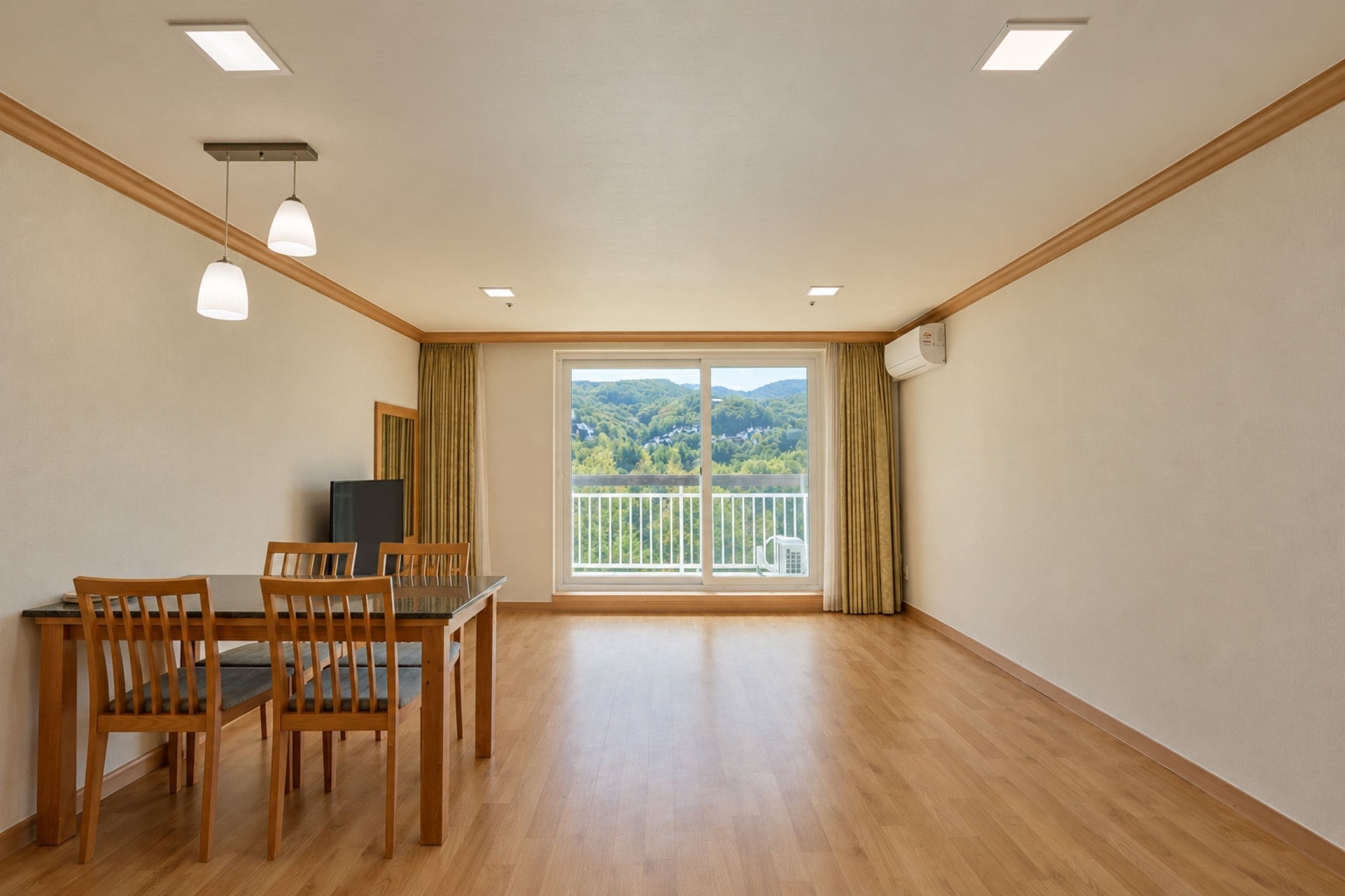 Quarto com uma mesa de jantar, cadeiras, televisão e varanda com vista para o verde.