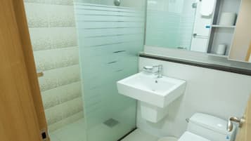 A bathroom with a glass shower enclosure, a white sink, and a toilet.