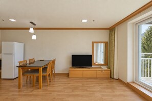 Una sala de estar moderna con comedor, televisor de pantalla plana y un amplio ventanal con cortinas.