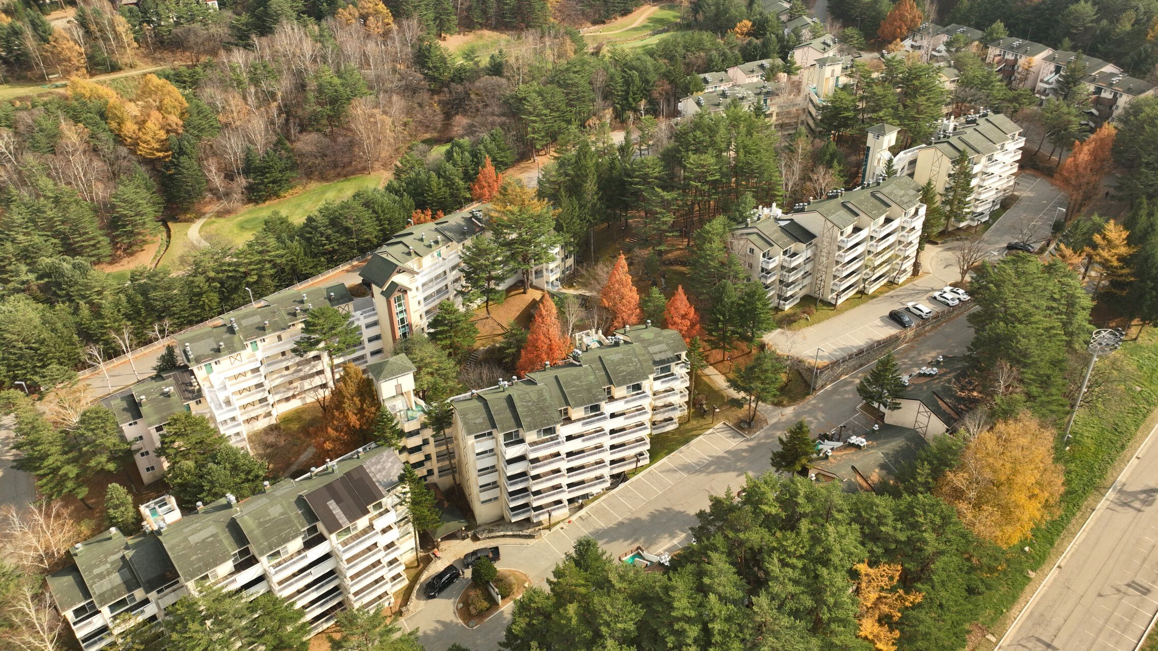 A residential area with multi-story buildings, a parking lot, and surrounding trees.