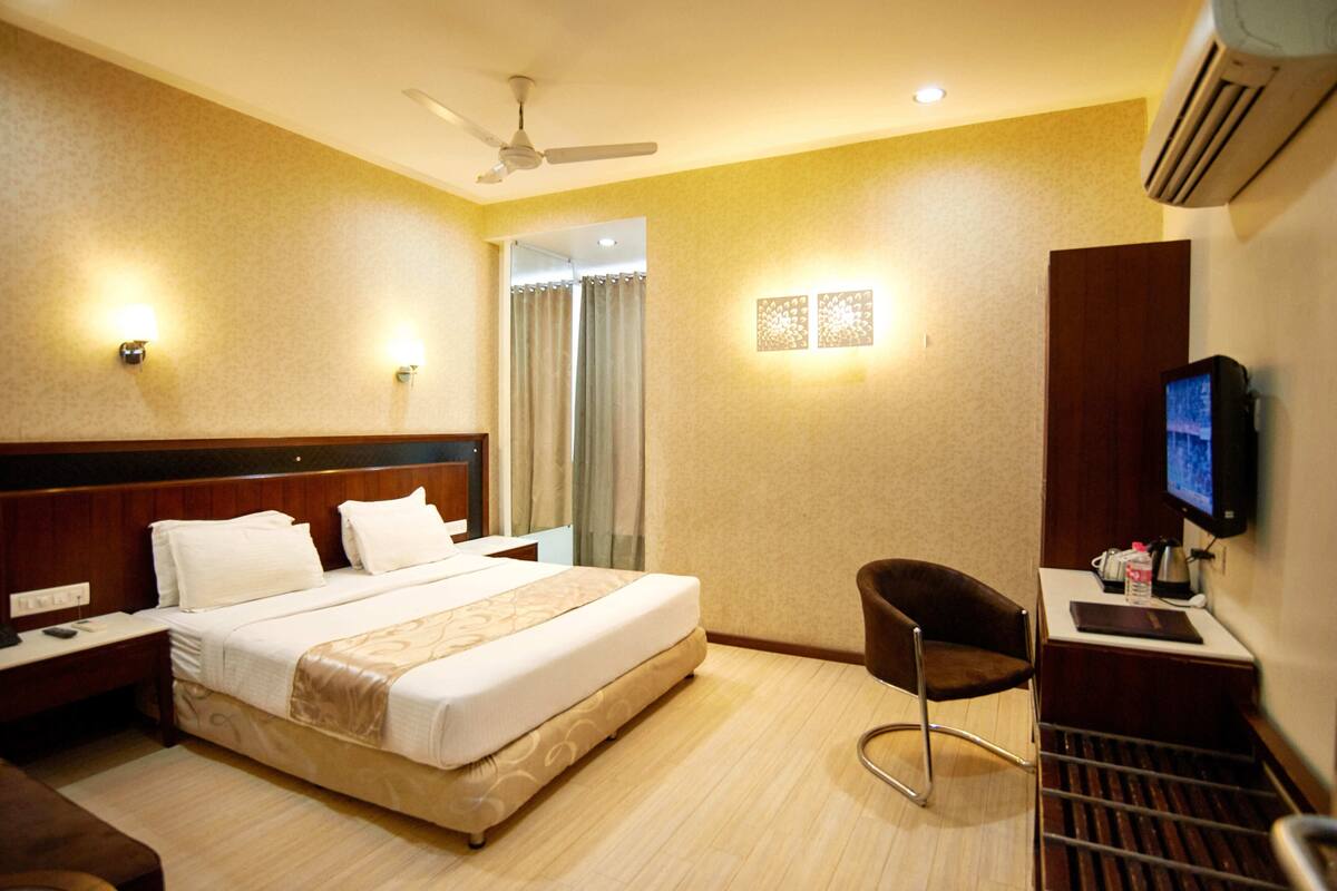 A hotel room with a bed, a desk with a chair, a TV, and a ceiling fan.