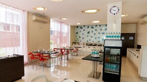 A modern hotel dining area with tables, chairs, a refrigerator, and a clock on the wall. - Hotel Sai Mahal (Rahata)