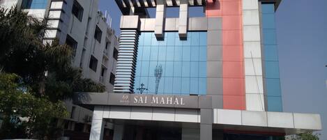 Exterior del Hotel Sai Mahal con un diseño arquitectónico moderno, destacando una entrada prominente y un cielo despejado.