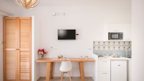 A compact kitchen with a wooden table, a white chair, a TV mounted on the wall, a microwave, and a small refrigerator. - Hermes Beach Front (Chania)